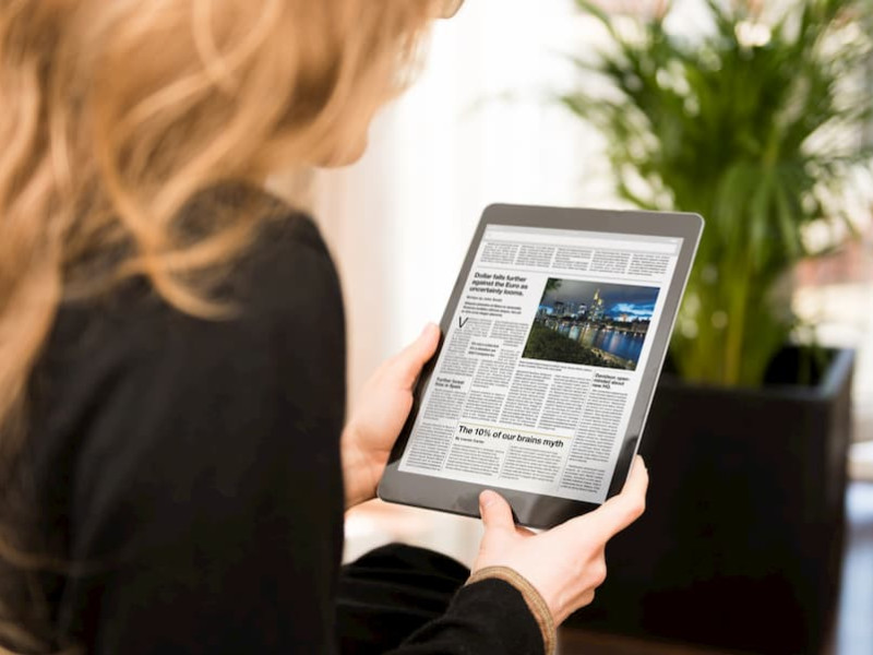 A woman reads an eNewspaper on a tablet.