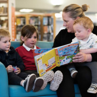 A mother reading to three young children in the library.