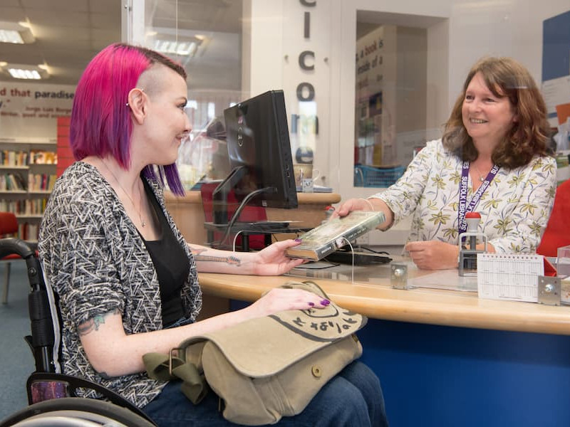 A library staff member handing a book to a customer at the counter