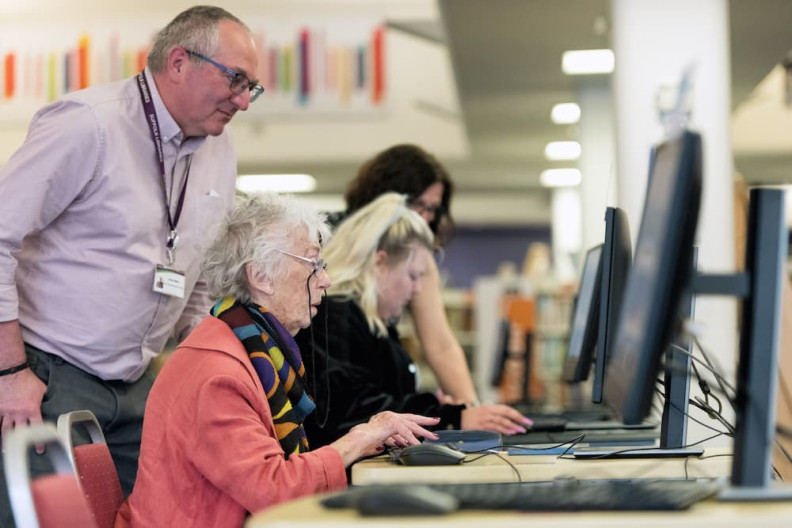 A library staff member helping a customer to use a computer