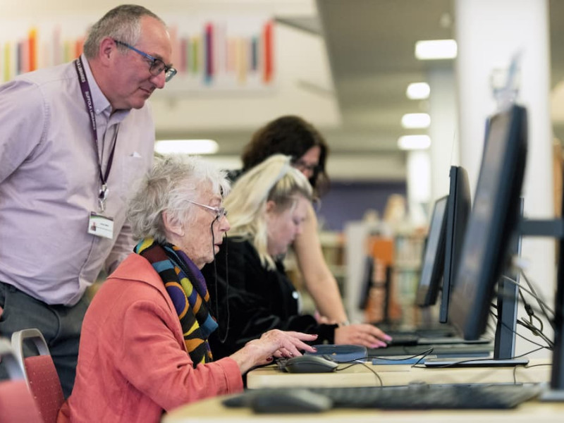 A library staff member helping a customer to use a computer