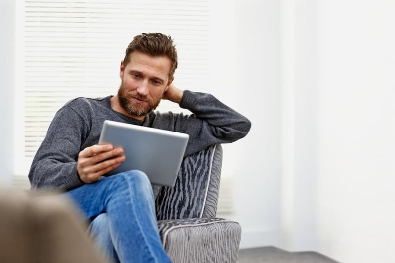 Man looking concentrated at an iPad while sitting on an armchair