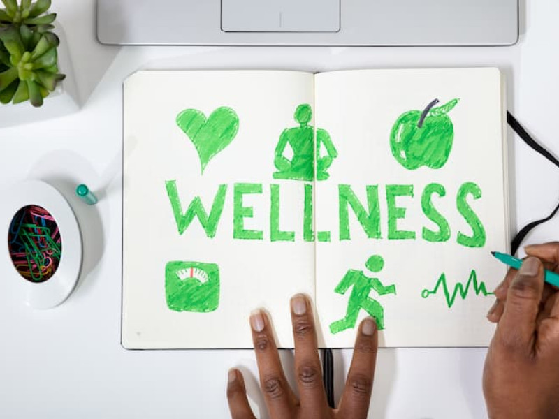 Wellness is written in a notepad with symbols of a heart, yoga, apple and a figure running.