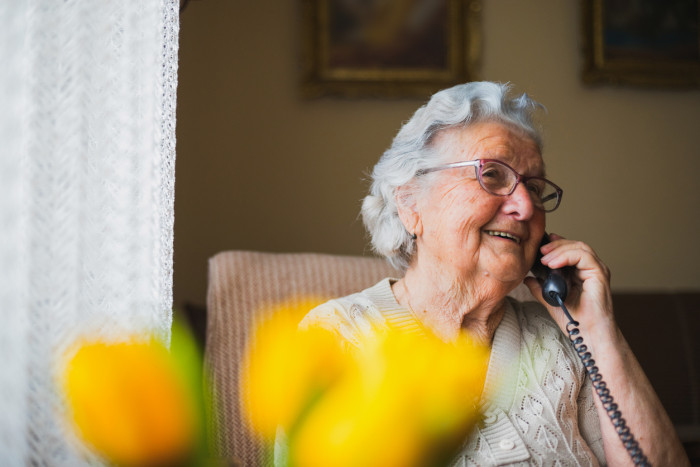 An elderly woman smiling and chatting on her landline