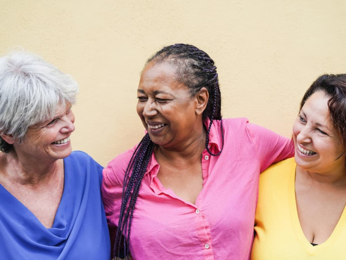 Three older women in colourful shirts with their arms around each other, smiling and laughing.